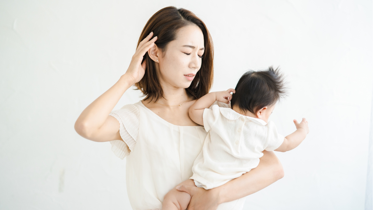 育児に疲れた母親が赤ちゃんを抱きながら悩んでいる様子。ワンオペ育児の大変さを表現した写真。