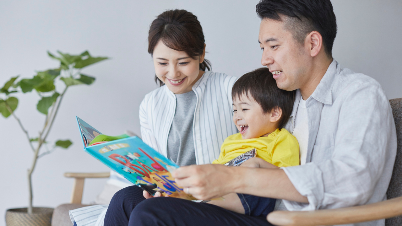 男性が育休中に家族と過ごす様子　絵本を楽しむ父親と子ども、母親の笑顔